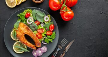 top-view-tasty-cooked-fish-with-fresh-vegetables-cutlery-dark-table_140725-143712